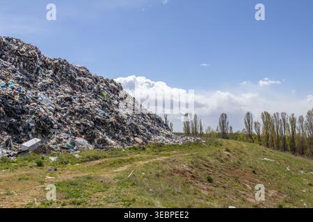 Une grande pile de déchets se trouve sur un site d'enfouissement pendant la journée. Des arbres sont présents à proximité, et le ciel montre quelques nuages. Cet endroit fait partie de déchets M. Banque D'Images