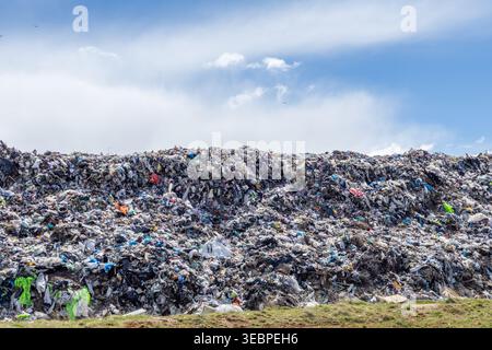 Les ordures et les déchets sont empilés haut dans un site d'enfouissement sous un ciel dégagé. La scène montre divers éléments mélangés dans les déchets, créant un grand Mo de poubelle Banque D'Images