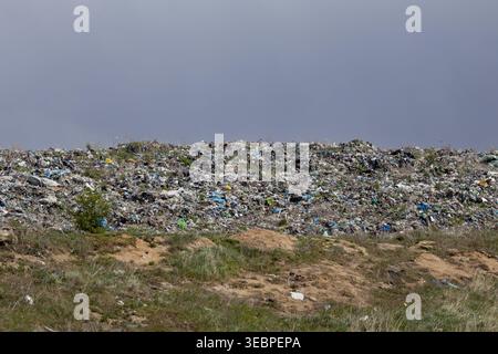Un grand site d'enfouissement est couvert de divers types d'ordures et de déchets. La zone montre des tas de déchets contre un ciel gris pendant l'après-midi. Banque D'Images