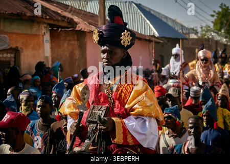 Zaria City, Nigeria - 22 mars 2026 : vue d'une figure royale dans d'opulents regalia rouge et or, menant une procession vibrante dans une rue animée. Banque D'Images