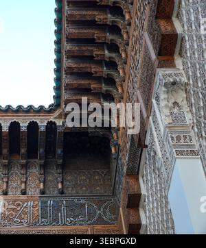 Corbeaux en bois sculpté ornés, arabesques en stuc et frise de calligraphie arabe dans une madrasa marocaine historique, Marrakech. Banque D'Images