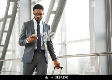 Homme d'affaires marchant dans un terminal de l'aéroport tout en vérifiant smartphone pour les mises à jour Banque D'Images