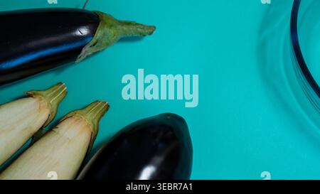 Aubergines entières et bol en verre transparent sur fond sarcelle — photographie de nourriture fraîche à plat d'aubergine Banque D'Images