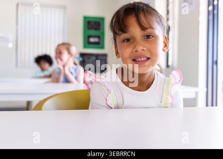 Camarades de classe féminines, enfant assis à la table blanche avant avec chaise jaune dans la salle de classe en haut rose Banque D'Images
