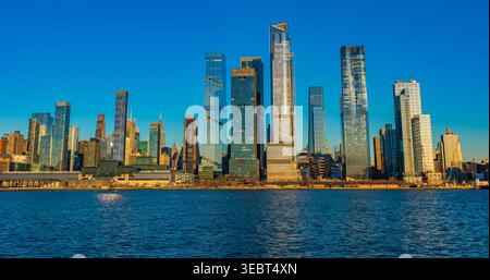 De l'autre côté des eaux calmes de la rivière Hudson, les tours Hudson Yards reflètent les couleurs vibrantes du crépuscule, mêlant modernité et charme urbain. Banque D'Images