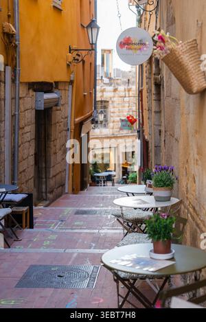 Café dans une allée ensoleillée et enseigne de parfumerie dans la ville historique de Grasse, France Banque D'Images