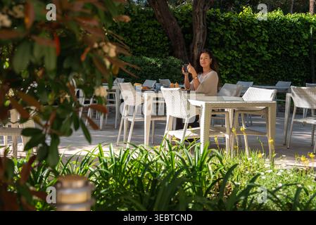 Femme à la terrasse ensoleillée d'un café à Antibes capture une photo de téléphone Banque D'Images
