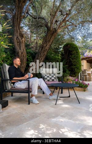 Homme se relaxant sur la terrasse du jardin avec olivier à Antibes, France Banque D'Images