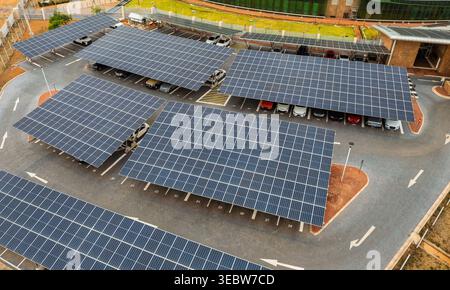 le plan à grand angle montre plusieurs rangées de panneaux solaires bleus fournissant de l'ombre pour les voitures garées dans un lot d'asphalte avec des flèches peintes en blanc et des marques. Banque D'Images