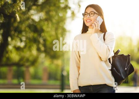 Jeune femme profitant d'une journée ensoleillée tout en parlant au téléphone dans un parc Banque D'Images