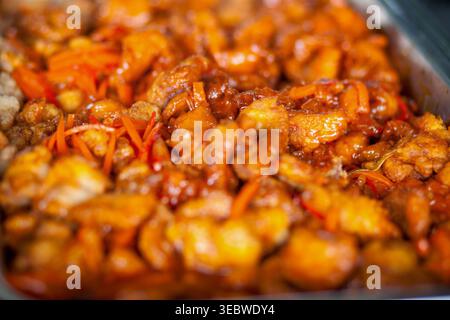 Gros plan détaillé sur des morceaux de poulet aigre-sucré croustillant et glacé accompagnés de carottes tranchées, servis sur un plateau de buffet en métal. Le Shallow de Banque D'Images