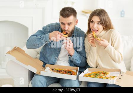 Jeune couple appréciant Pizza ensemble dans le salon confortable pendant la soirée décontractée Banque D'Images