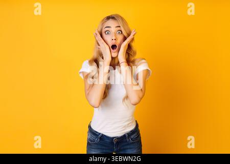 La femme surprise exprime le choc devant le fond jaune vif Banque D'Images