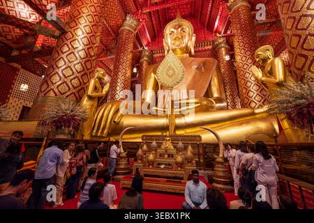 Phra Nakhon si Ayutthaya, Thaïlande - 30 mars 2025 : bouddhistes et dévots prient devant une statue dorée de Bouddha assis. Wat Phanan Choeng. Banque D'Images