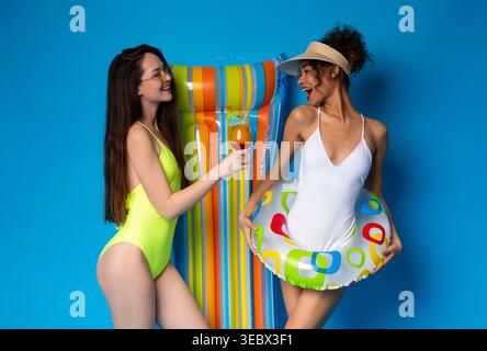 Amis profitant d'une journée d'été au bord de la piscine avec boissons et floaties colorées Banque D'Images