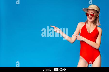 Jeune femme en maillot de bain rouge pose joyeusement sur un fond bleu Banque D'Images