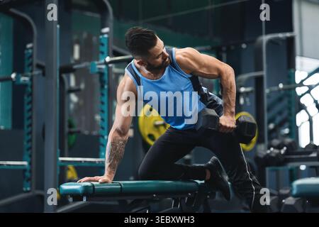 Homme soulevant l'haltère pendant la séance de musculation au gymnase dans l'après-midi Banque D'Images