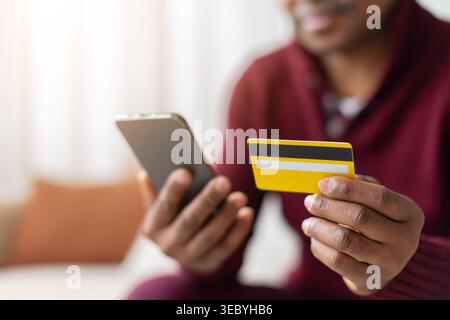Gros plan de mains d'hommes noirs tenant smartphone et carte de crédit à la maison Banque D'Images