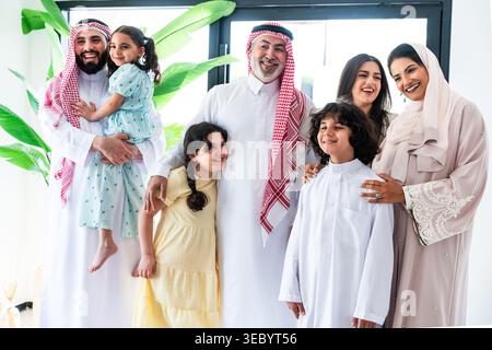 Famille arabe multigénérationnelle debout ensemble à la maison, souriant et embrassant à travers les générations, mettant en valeur les liens familiaux chaleureux, les vêtements culturels et Banque D'Images