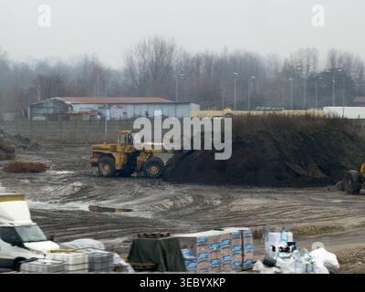 Katowice, Pologne - 3 décembre 2025 : la chargeuse sur pneus jaune lourde déplace la terre sombre et le sol d'excavatrice sur un site boueux pour un projet de construction industrielle Banque D'Images