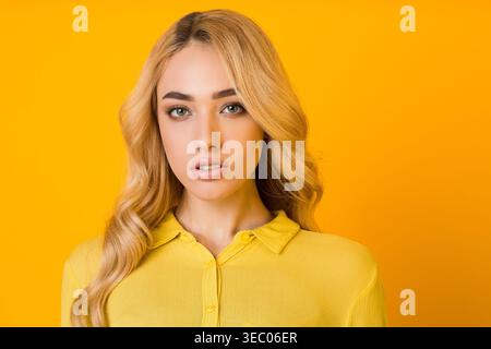 Jeune femme aux cheveux blonds portant une chemise jaune pose sur un fond jaune vif Banque D'Images