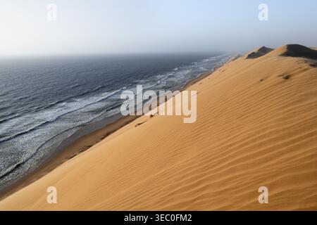Dunes de sable avec des modèles de vagues et la mer dans la lumière du soir, vent soufflant le sable à travers les dunes, côte atlantique et désert de sable avec mer de dunes, impressionnent Banque D'Images