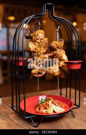 Une présentation attrayante de succulente poulet grillé tikka servi sur un stand innovant de style cage à oiseaux. Ce plat est parfait pour le bal de restaurant Banque D'Images