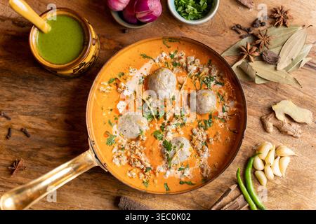 Ce cliché au-dessus de la tête présente un curry de boulettes de viande indien éclatant baigné d'une délicieuse sauce à l'orange crémeuse. Il est magnifiquement arrangé avec des herbes fraîches Banque D'Images