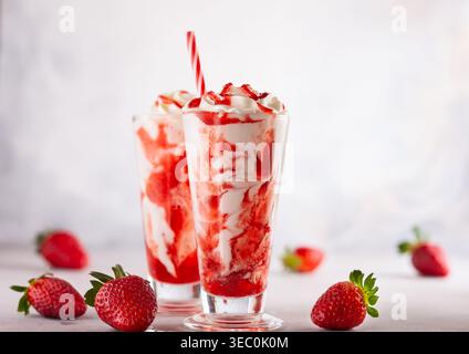 Milkshake aux fraises avec crème fouettée et sirop de baies dans le grand verre sur fond clair. Banque D'Images