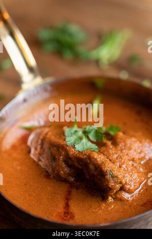 Ce gros plan détaillé se concentre sur la succulente pièce de viande immergée dans un curry de poulet ou de mouton épais et savoureux. La coriandre fraîche et le Chili fournissent vibra Banque D'Images