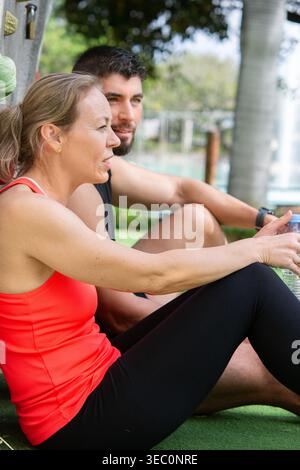 Fit couple assis et se reposer après l'entraînement à l'extérieur. Homme et femme prenant une pause, buvant de l'eau et récupérant après l'exercice dans un parc naturel en Banque D'Images