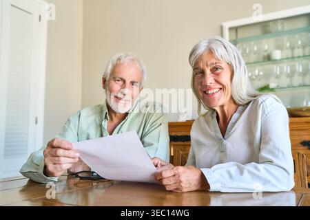 Planification de la retraite et sécurité financière — un couple de personnes âgées heureux examine des documents importants à leur table à la maison, souriant avec confiance à l'AC Banque D'Images