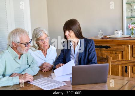 Planification de la retraite et protection financière — un couple de personnes âgées écoute attentivement une conseillère financière qui explique les documents sur un Banque D'Images