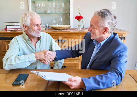 Planification de la retraite et sécurité financière. Un homme senior serre la main à un conseiller financier, finalisant un accord après avoir discuté de la succession et de l'intérieur Banque D'Images