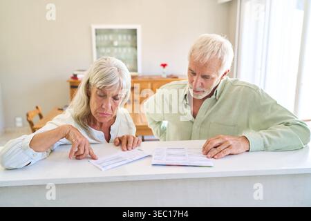 Planification de la retraite et protection financière — un couple de personnes âgées examine attentivement les documents financiers et les documents administratifs à une table à leur domicile. Banque D'Images