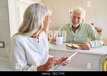 Un couple de personnes âgées est capturé dans une cuisine lumineuse, incarnant le vieillissement en bonne santé et l'inclusion numérique. Banque D'Images
