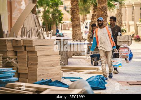 Marsa alam, egypte 21 avril 2026 : des ouvriers de la construction déplacent des matériaux de construction dans une rue de marsa alam, egypte, avec des panneaux de bois empilés dans le fo Banque D'Images