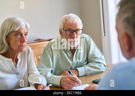 Planification de la retraite et protection financière — un couple de personnes âgées est engagé dans une discussion sérieuse avec un conseiller financier, examinant les documents pour es Banque D'Images