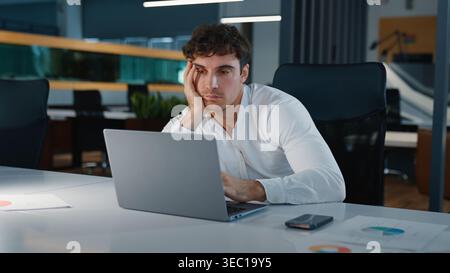 Ennuyeux somnolent fatigué homme d'affaires caucasien se sentant ennuyé à la recherche dans l'ordinateur portable homme d'affaires non motivé travailleur homme employeur Guy travaillant avec l'ordinateur Banque D'Images
