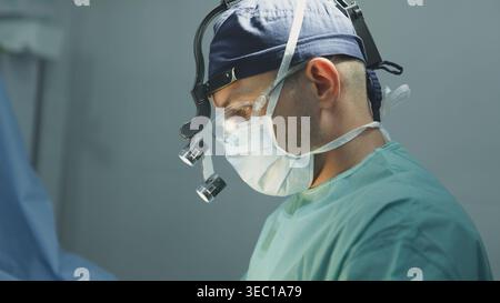 Gros plan chirurgien masculin dans le masque médical protecteur médecin homme portant des loupes de chirurgie innovantes avancées éclairage de travail clinique d'opération médecin Banque D'Images