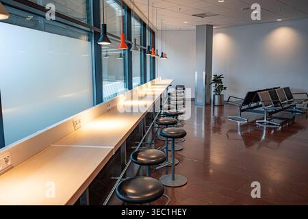 Le salon minimaliste de l'aéroport est doté d'un long comptoir de travail en bois avec prises de courant et de tabourets de bar noirs sous des lampes suspendues. Banque D'Images