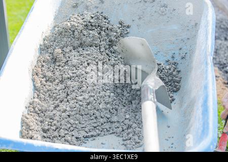 Gros plan d'un mélange de ciment et de mortier frais dans une brouette avec une truelle, montrant les matériaux de construction et les travaux de préparation sur un chantier de construction. Banque D'Images