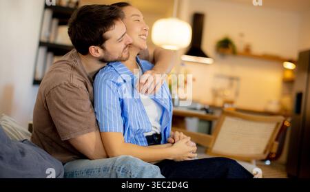 Un couple est assis près de chez eux. La femme sourit tandis que l'homme l'embrasse par derrière. Ils ont l'air heureux et détendu dans leurs vêtements décontractés. S Banque D'Images