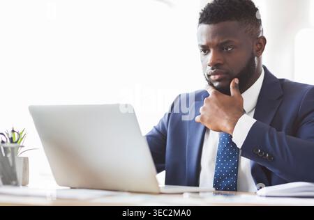Pensive african american young man working with laptop in office Banque D'Images