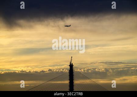 Silhouette d'un avion survolant le chantier de construction du pont Danjiang à New Taipei City, Taiwan, lors d'un coucher de soleil d'été doré. Banque D'Images