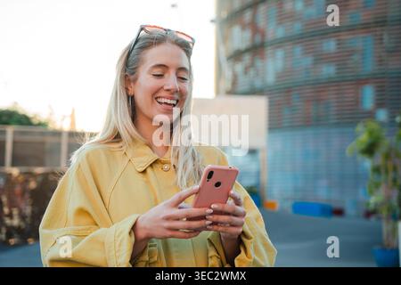 Jeune femme joyeuse s'engageant joyeusement avec son smartphone, affichant une expression de joie et de satisfaction alors qu'elle aime son temps libre à l'extérieur Banque D'Images