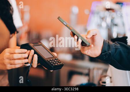 Barista adulte senior asiatique recevant un paiement mobile de la part d'un client utilisant un smartphone dans un café démontrant une transaction sans espèces moderne dans Cozy lo Banque D'Images