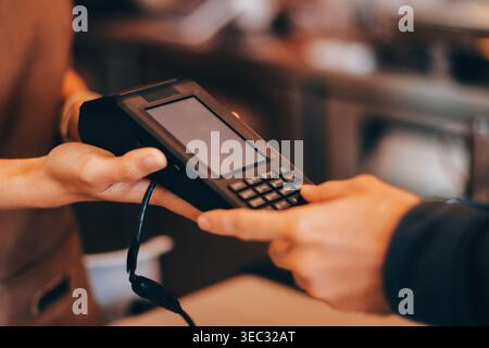 Barista adulte senior asiatique recevant un paiement mobile de la part d'un client utilisant un smartphone dans un café démontrant une transaction sans espèces moderne dans Cozy lo Banque D'Images