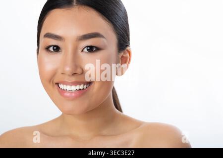 Femme souriante avec peau radieuse pose pour un gros plan sur un fond Uni Banque D'Images