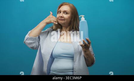 Femme tient une bouteille de savon avec pompe et fait un geste de la main de téléphone dans un studio ; promotion publicitaire d'hygiène ludique. Banque D'Images